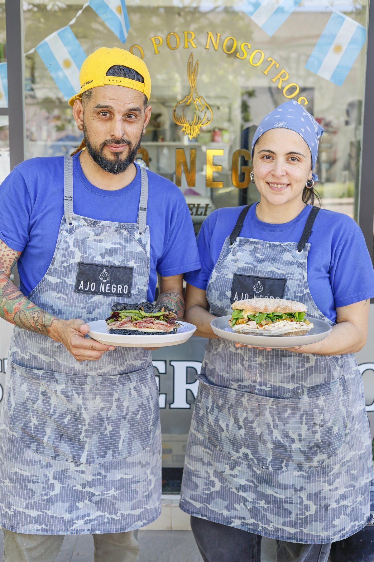 Equipo de Ajo Negro sostiene dos sándwiches frente al local.