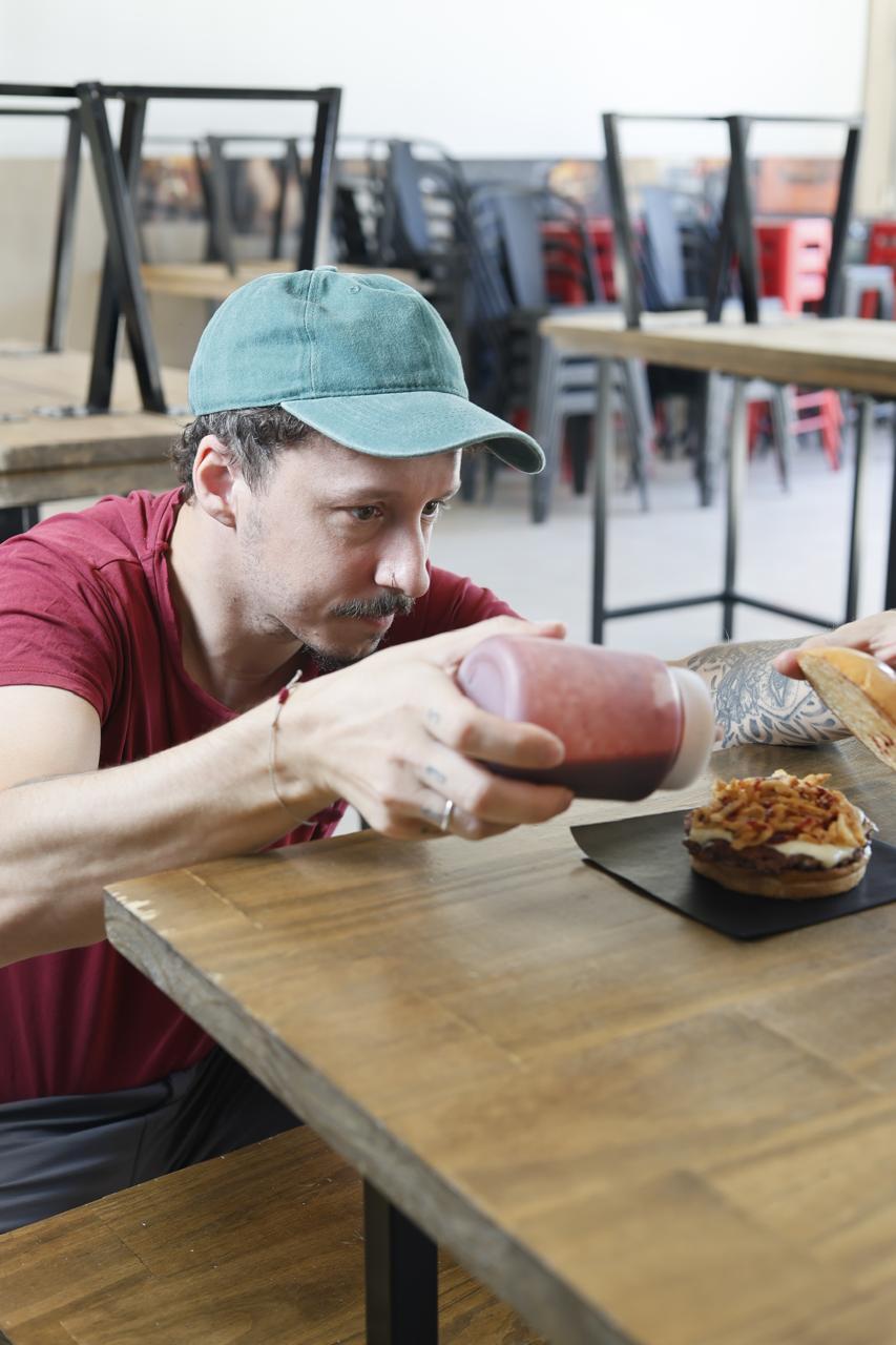 Integrante de Caos Burgers agrega salsa a una hamburguesa.